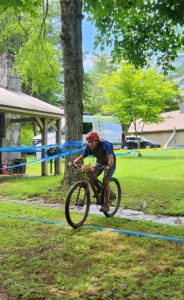 Author, covered in mud, riding bike across finish line.